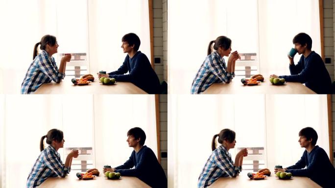 男人和女人喝茶聊天的侧视图，坐在厨房的桌子上一起享受宁静的早晨。饮料和人的概念。
