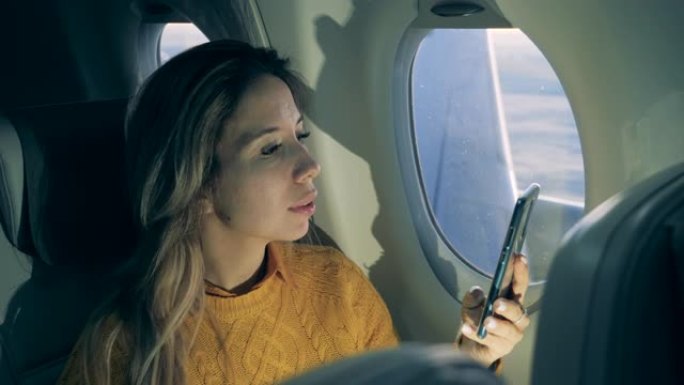 华丽的女士在飞机上飞行时正在使用手机