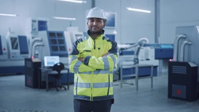 穿着安全背心和安全帽的英俊印度工程师的肖像交叉双臂微笑。在现代制造工厂工作的职业女性。具有数控机械和