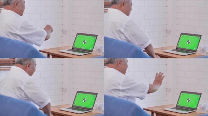 亚洲老爷爷在家用电脑看绿屏到视频会议。家里绿屏