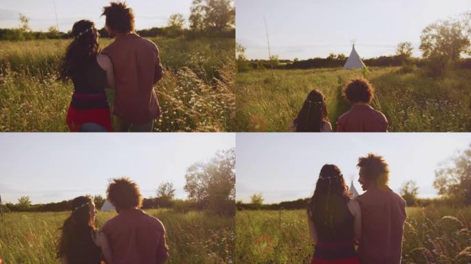 年轻夫妇在野营度假时穿过田野走向圆锥形帐篷的后视图 -- 慢动作拍摄