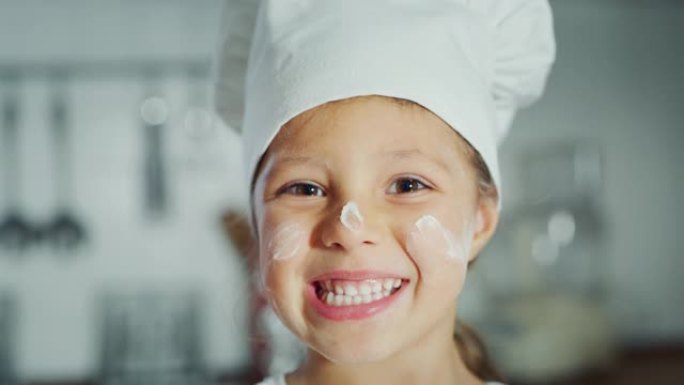 一个戴着厨师帽的漂亮小女孩 (孩子) 对着镜头微笑，脸上脏了食物。
