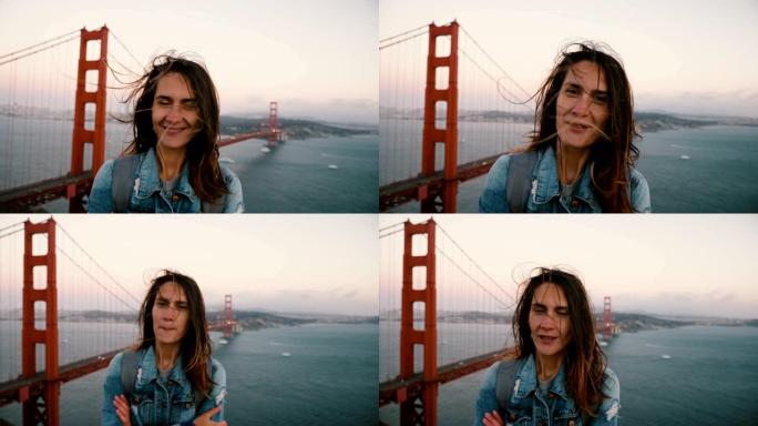 在著名的日落金门大桥，快乐的旅游女人的惊人生活方式肖像，头发在强风中吹动。
