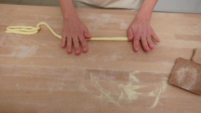 女人的手将意大利面面团卷成厨房柜台上的绳子
