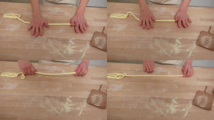 女人的手将意大利面面团卷成厨房柜台上的绳子