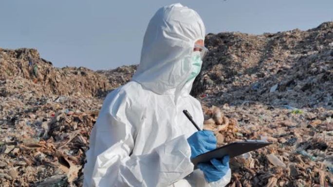 亚洲女科学家拿着剪贴板，穿着化学防护服病毒COVID-19.Biologists在废物中进行研究电晕