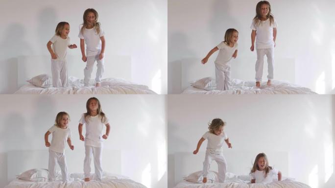 两个姐妹穿着白色睡衣，跳上床，玩得很开心。