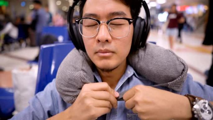 亚洲男子使用旅行颈枕在机场用耳机小睡
