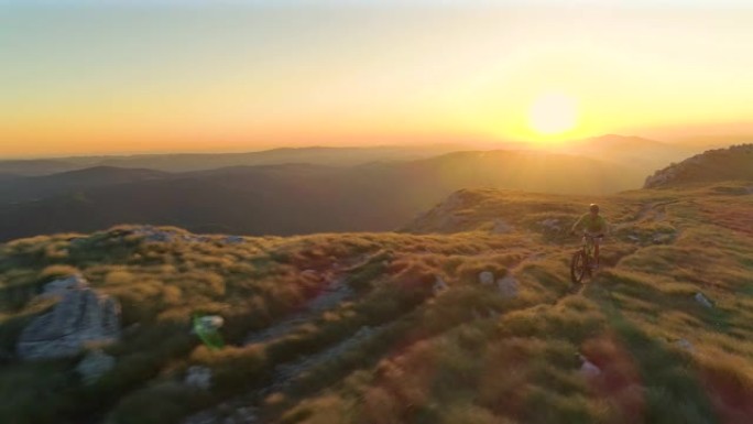 无人机: 金色傍晚的阳光照耀着骑自行车的山地车手。