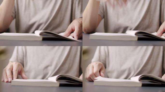 亚洲人呆在家里一边看一本非小说类的书。他翻开学习书的一页。成年男子用手指指着一本书。