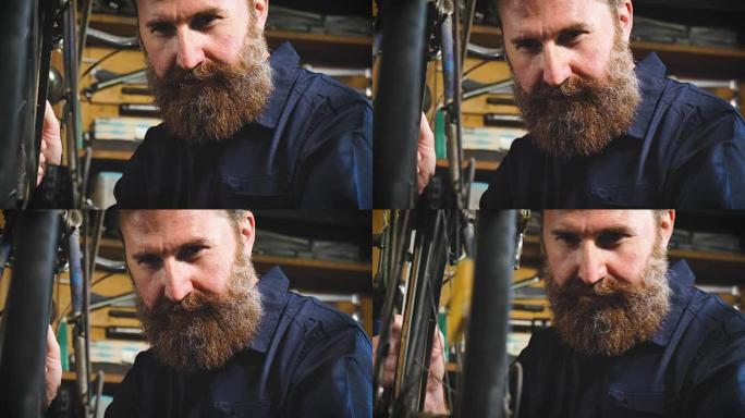 穿着整齐的英俊大胡子的时髦大师，自行车专家，在他的车间修理自行车，车轮，框架，辐条，工具的背景。