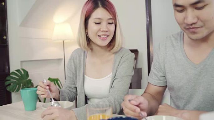 快乐甜蜜的亚洲夫妇在早上醒来后吃早餐、牛奶麦片、面包和喝橙汁。丈夫和妻子一起吃饭。