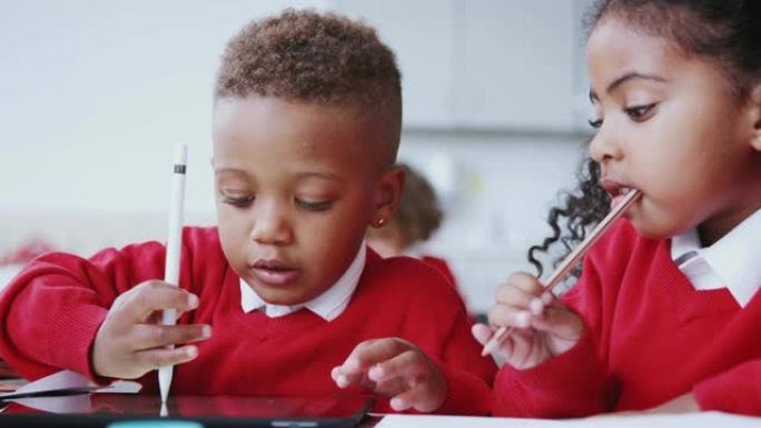 一个男孩和女孩在婴儿学校教室的桌子上使用平板电脑和手写笔，特写