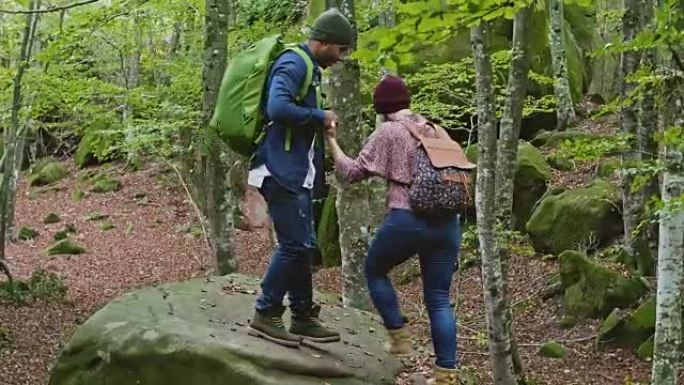 男人协助女人在森林的巨石上行走