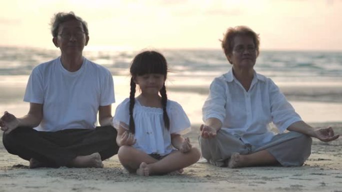 祖父母和孙女在沙滩上做瑜伽以日落冲浪的剪影。家庭，生活方式，人，人寿保险，多代，老人，假期，关系，孩