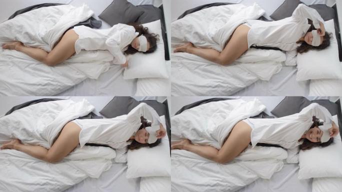 穿着男装衬衫和睡眠面具的调情女人在床上对着镜头微笑