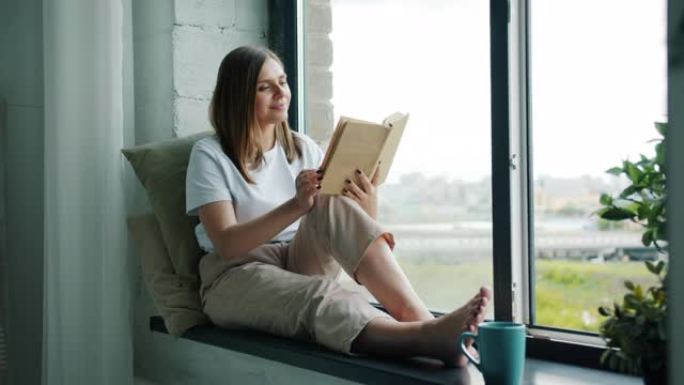 漂亮的年轻女士在窗台上看书，微笑着看着外面