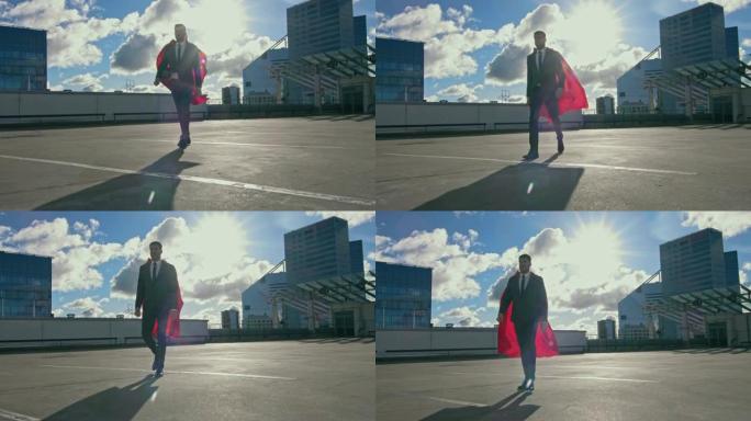 商人超人带着红色披风在风中行走在摩天大楼的屋顶上，准备拯救这一天。在现代市中心的背景中。在低角度拍摄