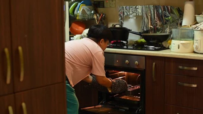 一名亚洲中国中年妇女在厨房烘烤准备饭菜时从烤箱中拉出蛋糕盘