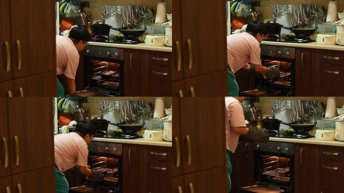 一名亚洲中国中年妇女在厨房烘烤准备饭菜时从烤箱中拉出蛋糕盘
