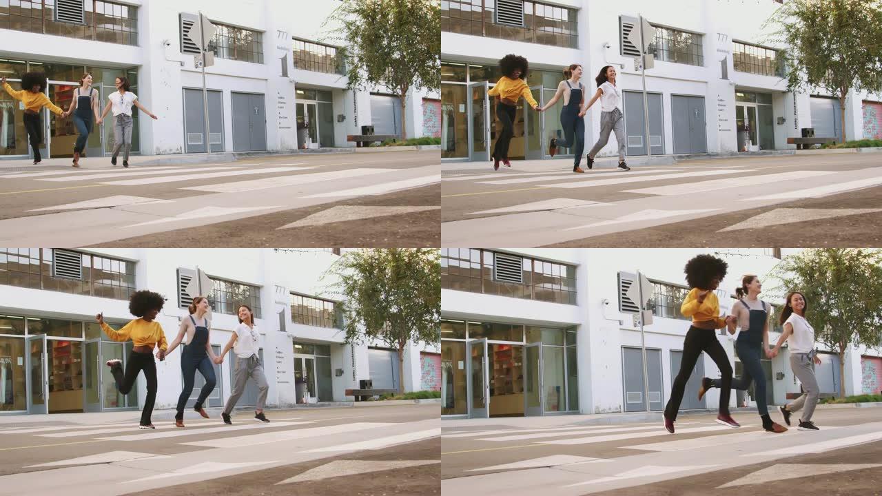 三个千禧一代的女友在穿过人行横道时手牵手大笑