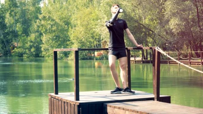 一个人站在池塘附近，用假肢喝水。4K。