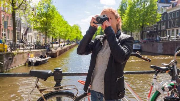 在阿姆斯特丹旅行的女游客，在美丽的晴天用老式模拟相机拍摄运河照片