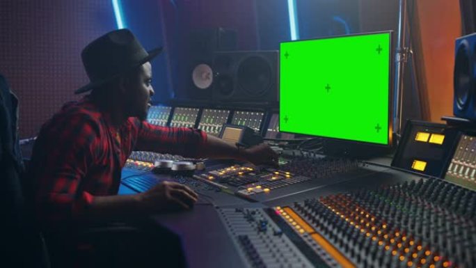 在音乐录音室工作的时尚音频工程师的肖像，使用绿屏计算机，混音器板，控制台来创作新歌。富有创造力的黑人