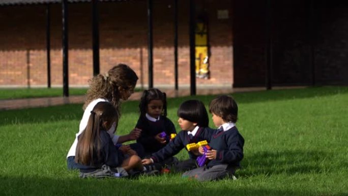 拉丁美洲教师和年轻学生在学校操场上玩建筑积木