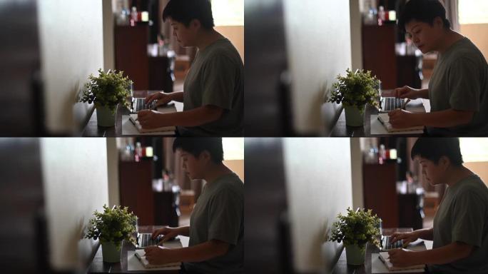 一名在家里工作的亚洲中国女性中年成年人使用她的笔记本电脑和写笔记