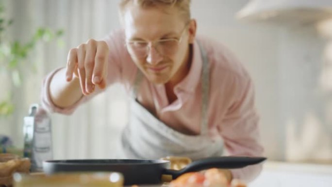 英俊的年轻人在煎锅上准备健康的素食。在现代厨房里撒上健康的绿色食品和香料。天然清洁饮食和健康的生活理