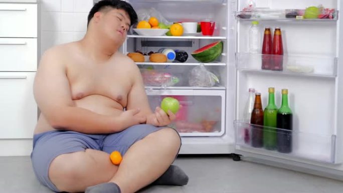 超重的人打开冰箱，吃晚饭，坐在冰箱前睡觉。真实的身体