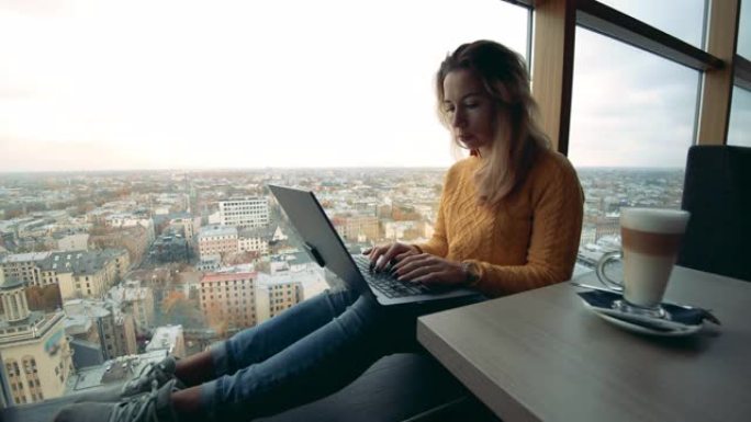 一位女士正在全景窗户旁边的笔记本电脑上工作