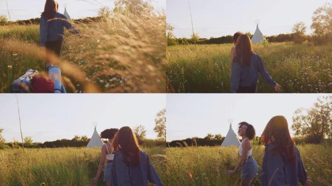 两个女性朋友在野营度假中穿过田野走向圆锥形帐篷的后视图