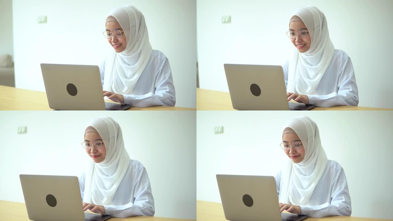 微笑的年轻穆斯林妇女在家里使用现代笔记本电脑的肖像