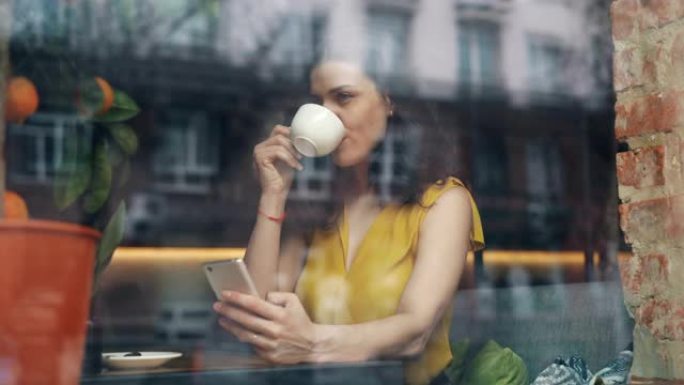 可爱的女学生在舒适的咖啡馆喝咖啡和使用智能手机
