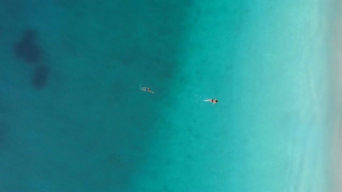 男人和女人在地中海清澈透明的绿松石水中游泳。空中自上而下的射击