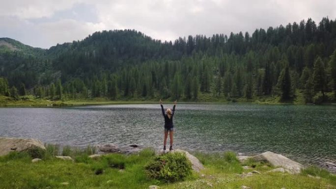 徒步旅行时，一个湖泊和一个美丽的女人的航拍图像，步行后到达目的地，并为实现目标而感到高兴。