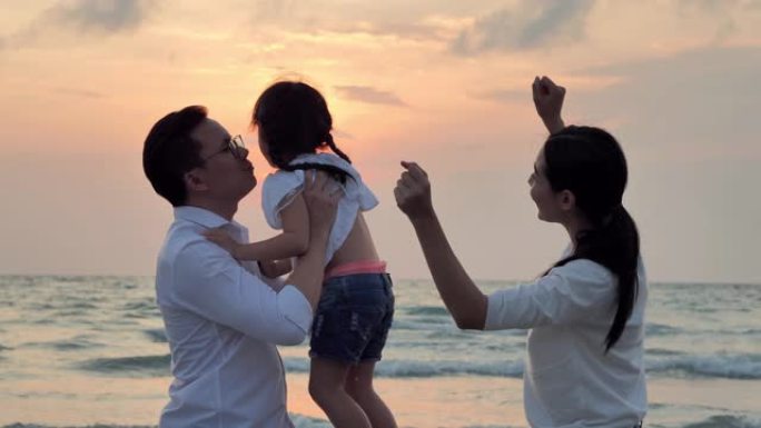 剪影快乐的父亲、母亲、女儿在沙滩上沿着日落海浪的边缘玩得开心。积极的父母和人们在暑假与孩子一起户外活