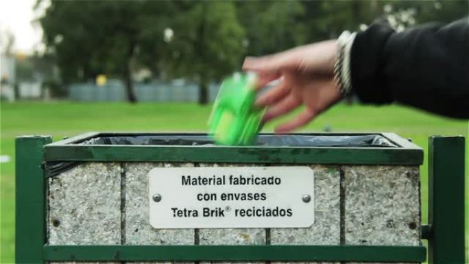 年轻人把一个罐扔进公园的回收箱。