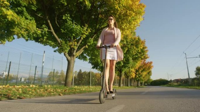 低角度: 千禧一代乘坐电动滑板车沿着道路行驶，穿过秋天的彩色树木。