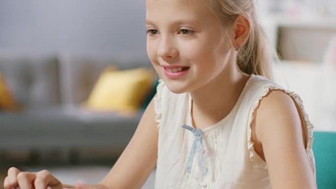 可爱的小女孩坐在客厅的桌子旁使用笔记本电脑。孩子在浏览互联网并观看卡通和有趣的视频时很有趣。