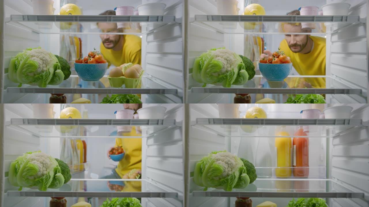 厨房冰箱内的摄像头: 英俊的男人打开冰箱门，里面看着盒装鸡蛋。准备健康餐的人。从装满健康食品的冰箱拍