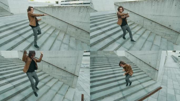 开朗快乐的长发年轻人在走下楼梯时积极跳舞。他穿着一件棕色皮夹克。在商务中心旁边的城市混凝土公园拍摄的