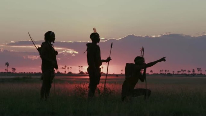 在博茨瓦纳的Makgadikgadi草原上，夕阳下三名桑族人/丛林人穿着传统服饰寻找动物的4K壮观的