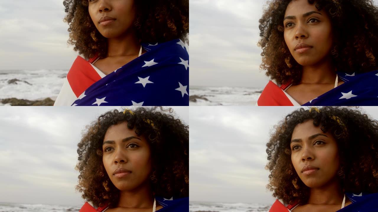 站在海滩上的美国国旗包裹着的非裔美国妇女的前视图4k