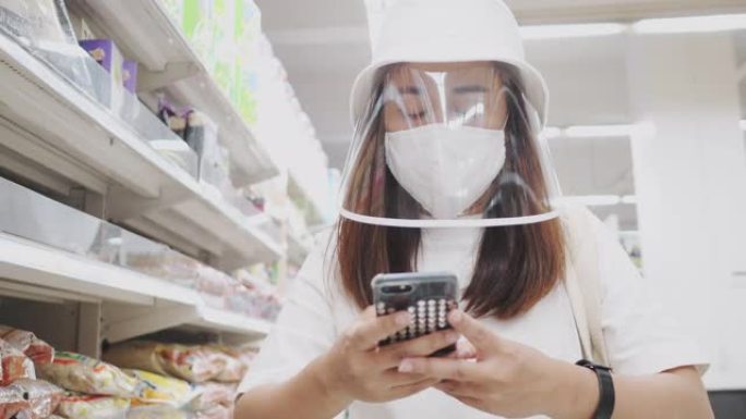 2019冠状病毒病的影响:亚洲妇女戴着防护口罩推着购物车在超市里行走