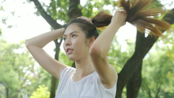 运动年轻的亚洲妇女在早晨在城市公园跑步前拉直头发。运动健康生活方式理念。