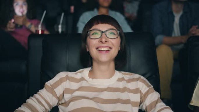 戴着眼镜的漂亮年轻女士的慢动作在电影院里笑着看电影