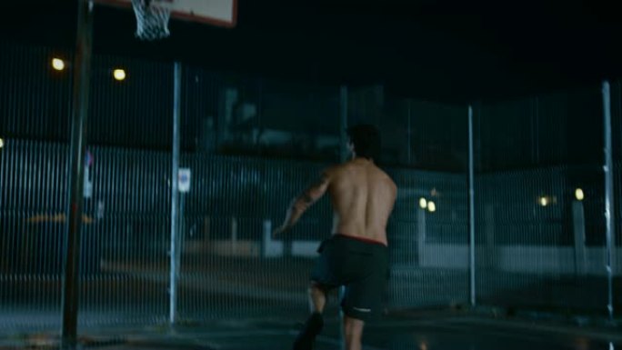 运动年轻的男子篮球运动员运球并在围栏的街球场上扔球。居民区雨后的夜间录像。